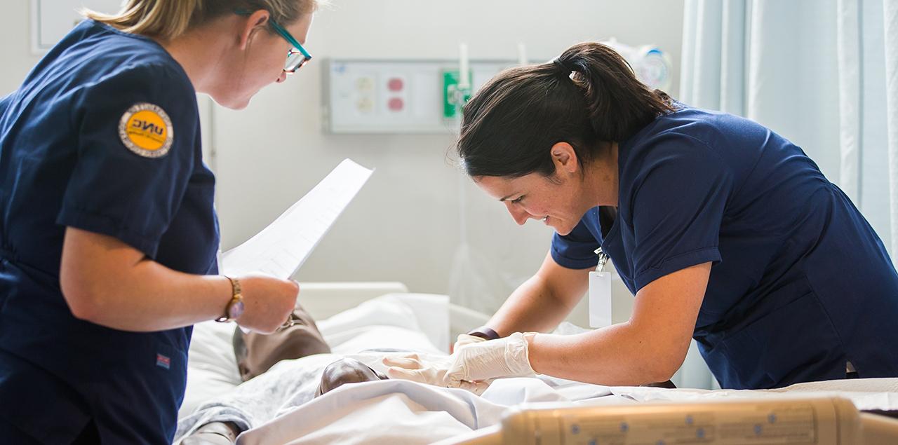 两个女护生在床上照顾一个人体模型病人